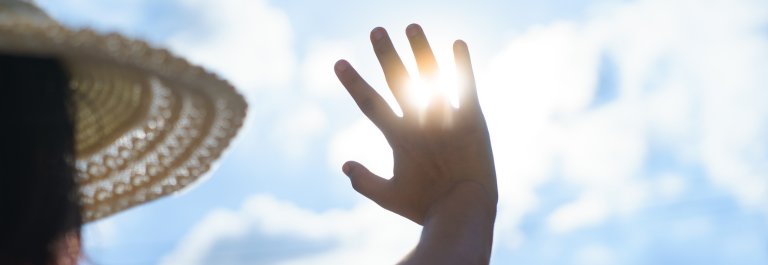 person in sun hat holding hand up to block the sun