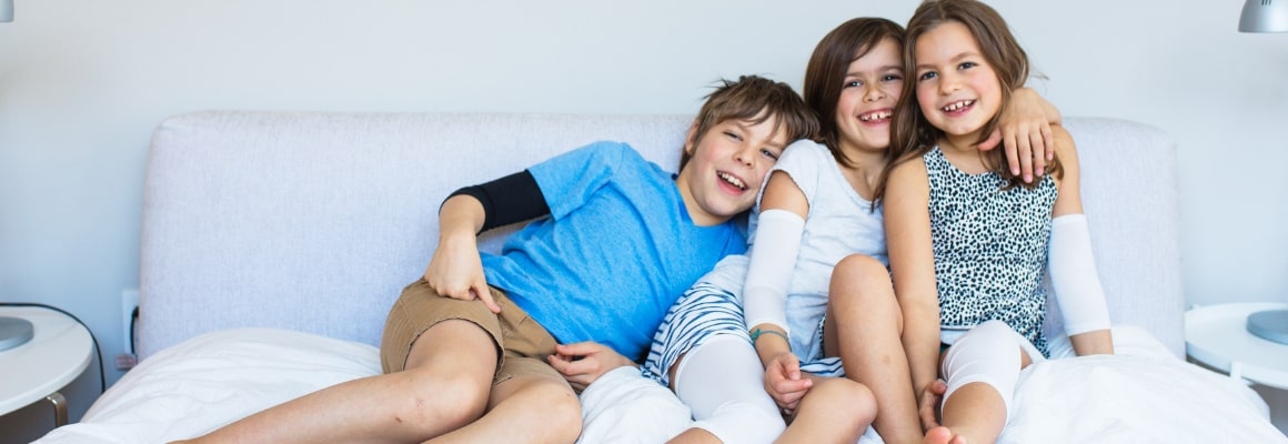 Two boys and one girl leaning on each other while laughing and smiling and sitting on a bed.