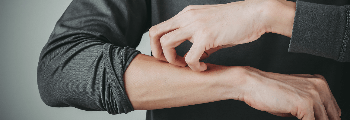 man in grey shirt scratching arm