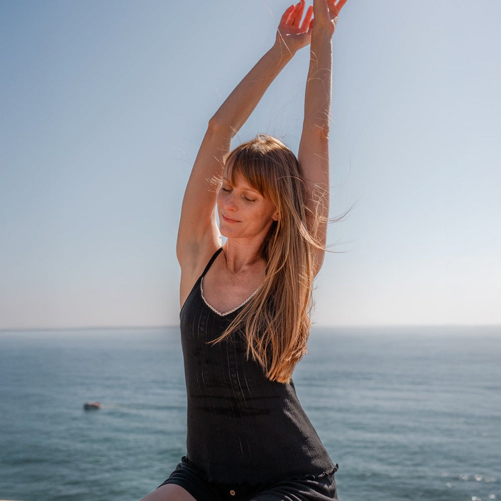 Woman stretching by the ocean in a black tank top, breathable cotton that keeps skin cool