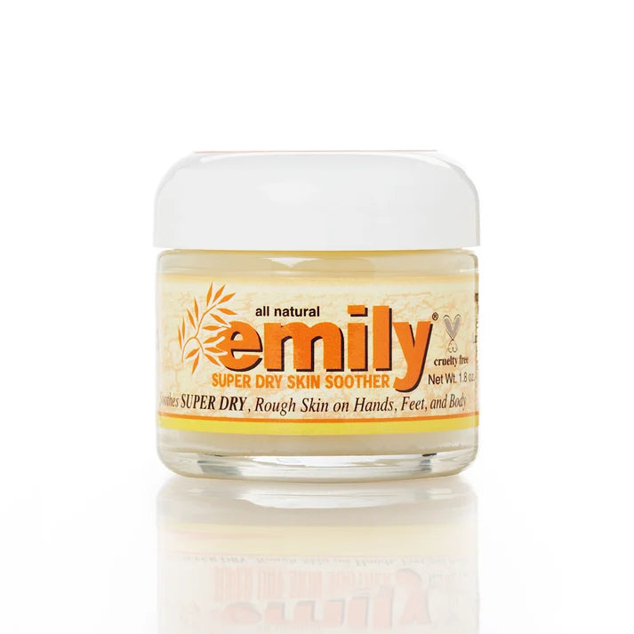 A jar of Emily Super Dry Skin Soother cream on a white background with a soft reflection below. The jar is clear glass showing a pale yellow cream inside, with a white lid and a label featuring orange and black text.