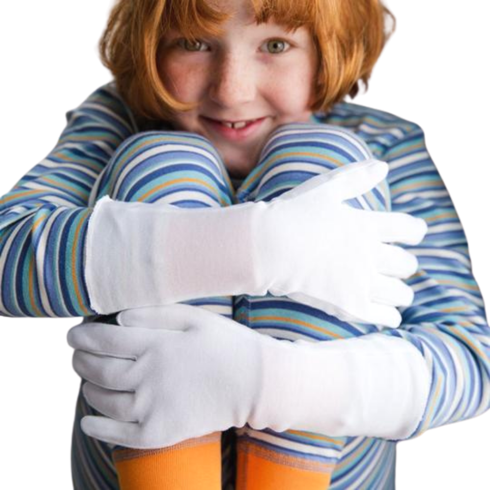 Girl in blue striped pajamas hugging knees to chest and wearing white cotton gloves.