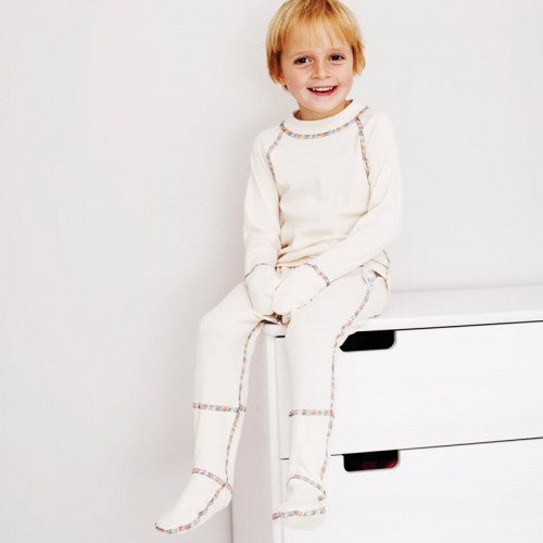 Boy wearing a matching top and pants in natural white with rainbow piping.