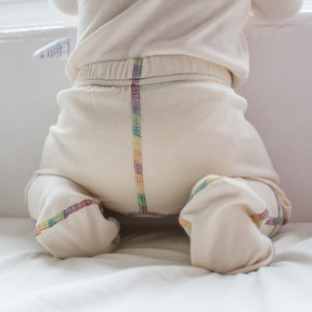 Close up of the back of the organic cotton footed pants for kids showing rainbow piping and natural white fabric.