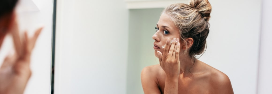 woman looking in mirror putting cream on face