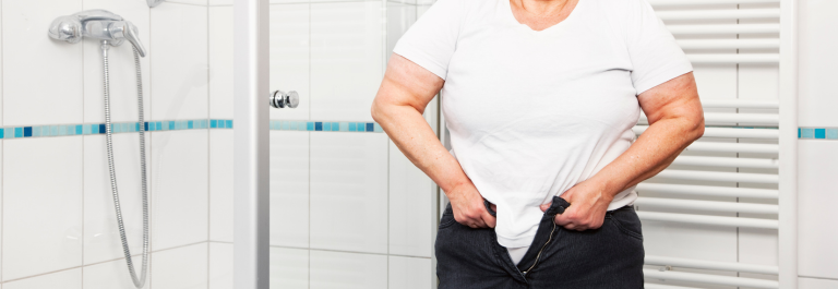 woman in white shirt struggling to put on jeans due to weight gain 