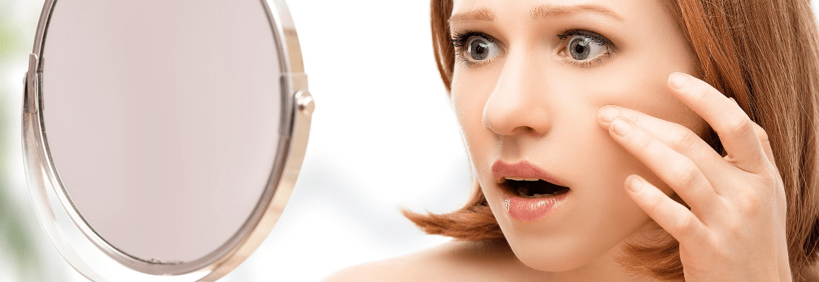 red haired woman looking in handheld mirror in shock