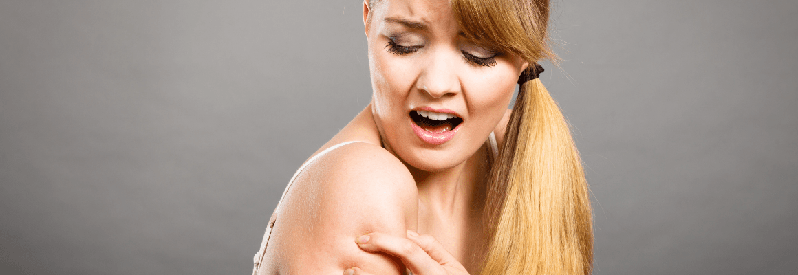 woman scratching shoulder against grey background
