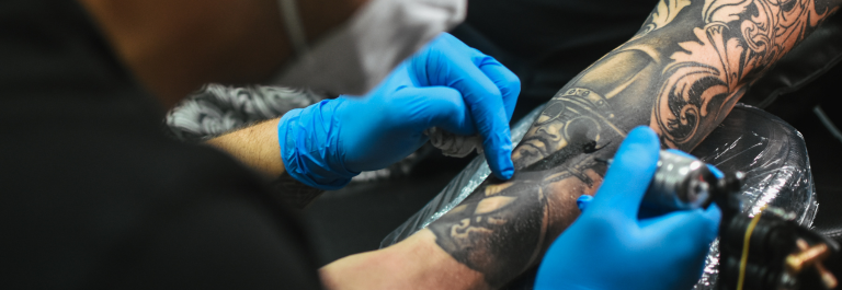 tattoo artist in blue latex gloves tattooing someone