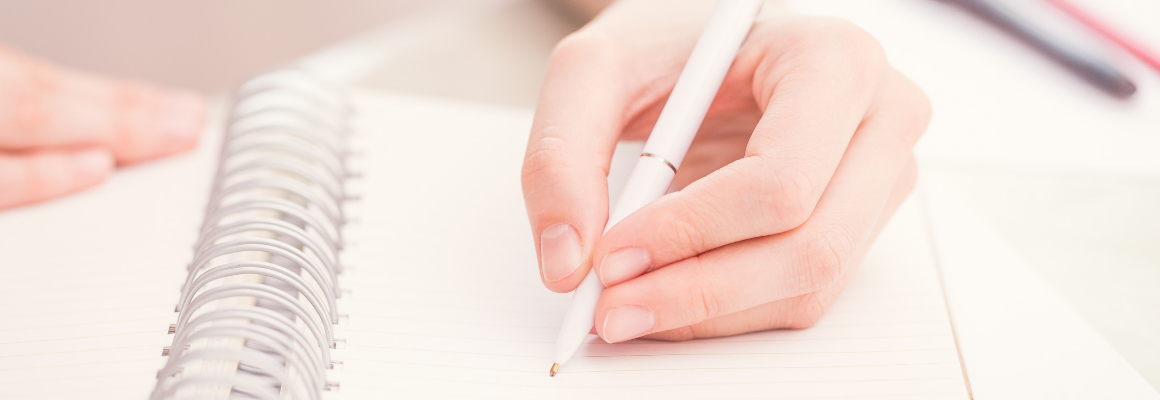 person holding pen and writing in journal