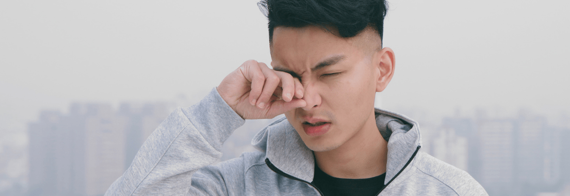 man in grey hoodie rubbing eye