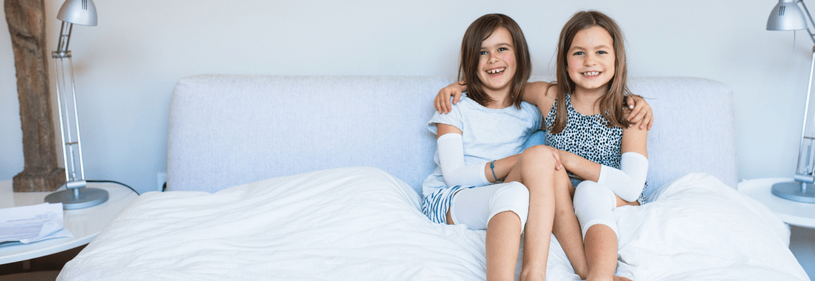 two little girls sitting on bed wearing eczema bandages