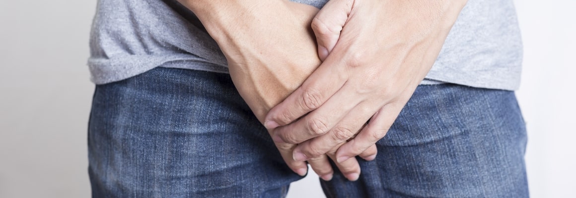 Man in jeans with hands covering the scrotum area.