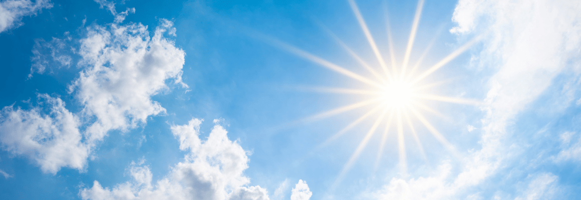 Fluffy white clouds in a bright blue sky with the sun shining.