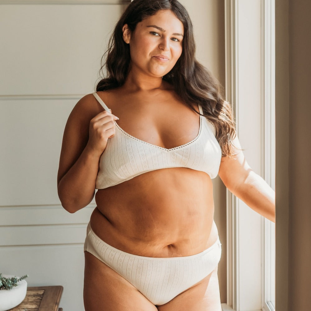 Curvy woman by a window in a natural pointelle bikini set, eczema-safe organic cotton