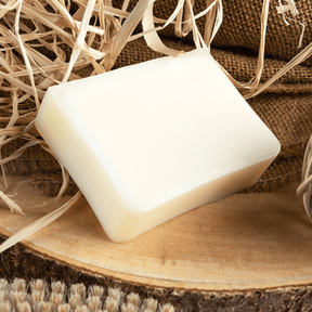 tallow bar of soap sitting on a wooden tree stump and hay and a burlap bag.