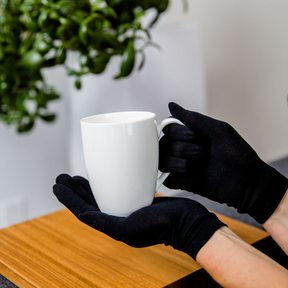Hands holding a white mug while wearing black Remdywear gloves for adults.