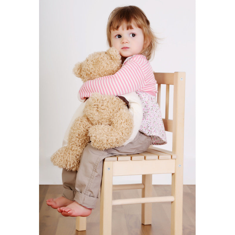 Toddler girl squeezing a teddy bear and sitting on a wooden chair while wearing her pink and white striped cotton scratchsleeves with scratch mittens.