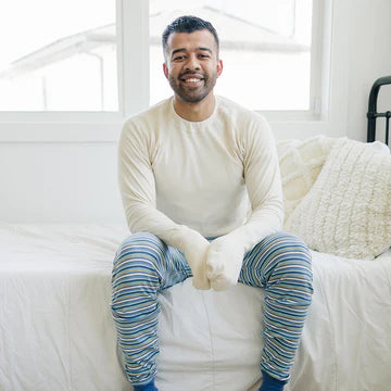 Man sitting on bed with a white mitten top and blue striped pants.