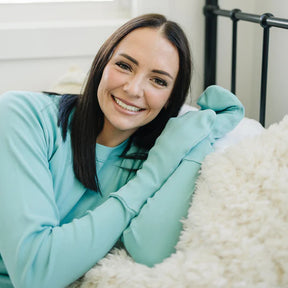 Woman laying down and smiling while wearing a light teal top with mittens.