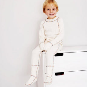 Boy wearing a matching top and pants in natural white with rainbow piping.