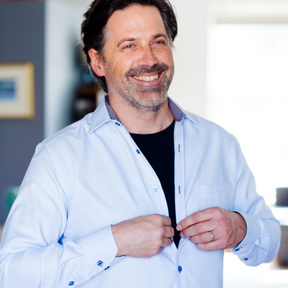 Man smiling while wearing a black Remedywear shirt underneath a business shirt he is buttoning up.