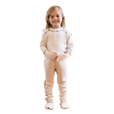 Toddler girl standing and wearing the one piece footie with closed mittens in cream with rainbow piping.
