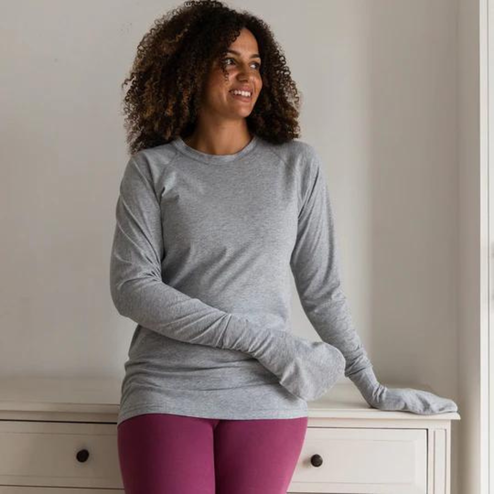 Woman standing while wearing a grey cotton top with closed eczema mittens for adults.