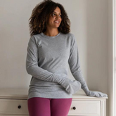 Woman standing while wearing a grey cotton top with closed eczema mittens for adults.