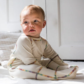 Baby sitting on floor while wearing the cream colored 100% organic cotton one piece footie with closed mittens.
